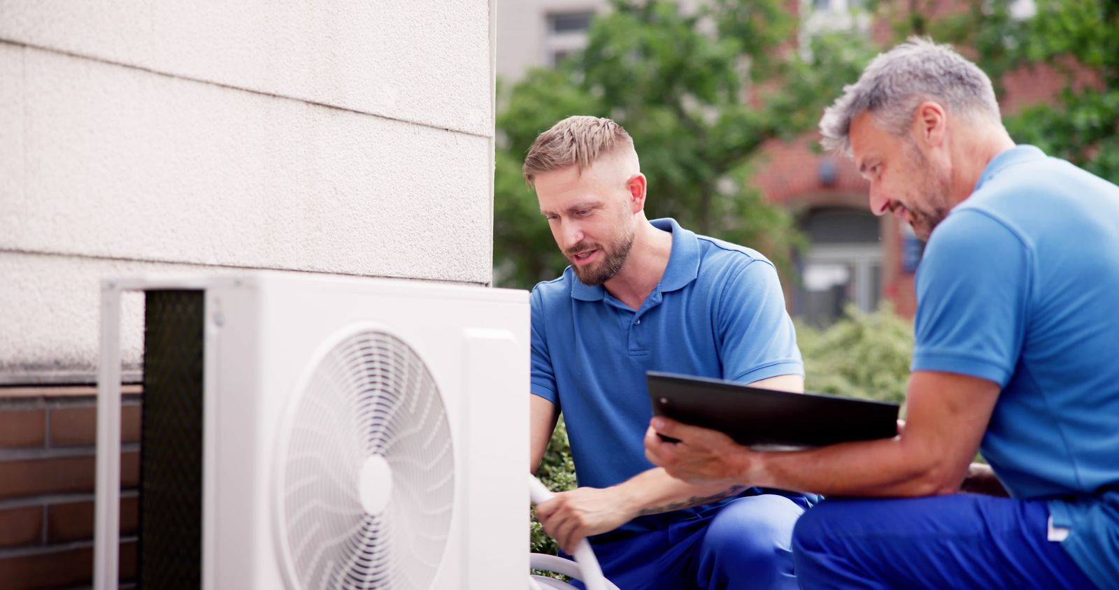 Two HVAC technicians reviewing a clipboard beside an outdoor heat pump